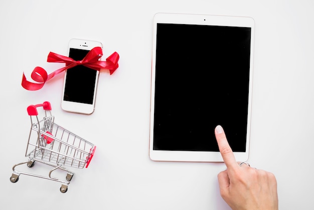 Hand on tablet near smartphone and shopping trolley