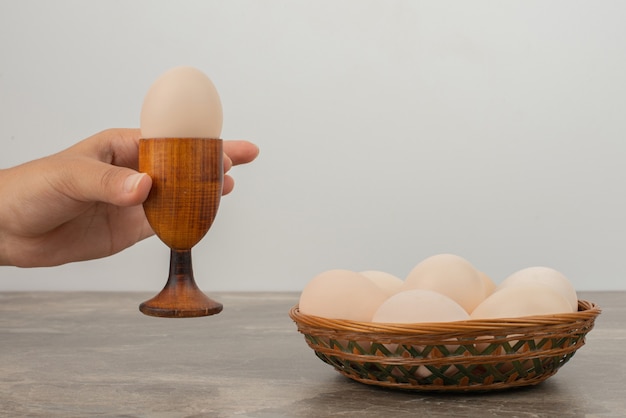 Hand taking a cup of egg and basket of white eggs .