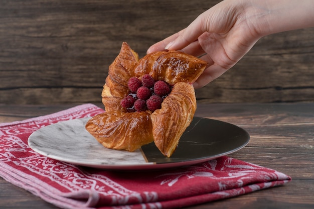 Hand taking fresh raspberry pastry from wooden table.