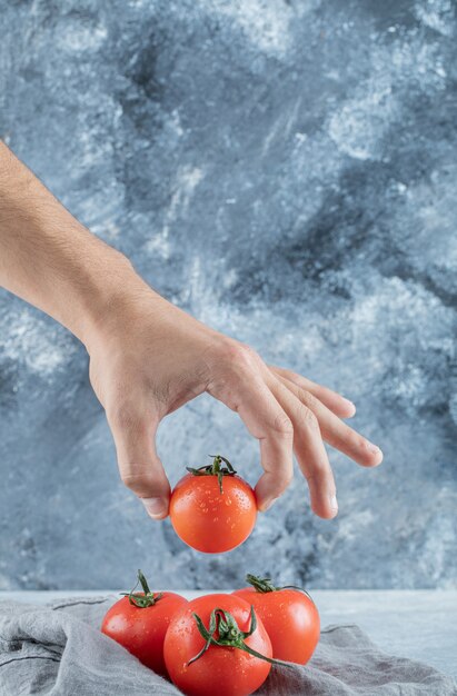 Hand taking a fresh whole tomato on a gray wall.