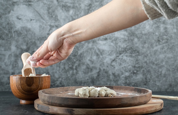 Hand taking a pinch of flour from a wooden bowl on gray.