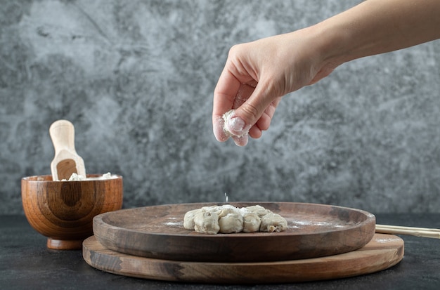 Hand taking a pinch of flour from a wooden bowl on gray.