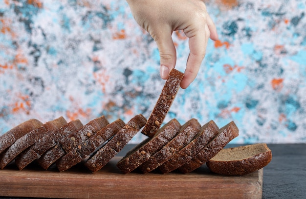 Foto gratuita mano che cattura una fetta di pane fresco sulla tavola di legno.