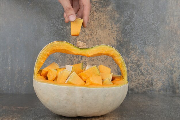 Hand taking a slice of pumpkin from ripe pumpkin on marble wall.