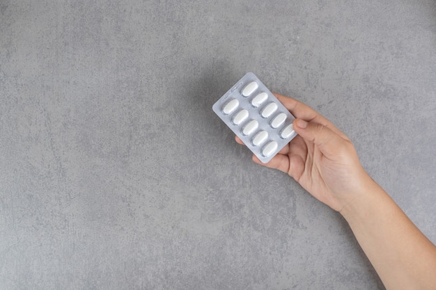 Hand taking a white pill on a gray surface