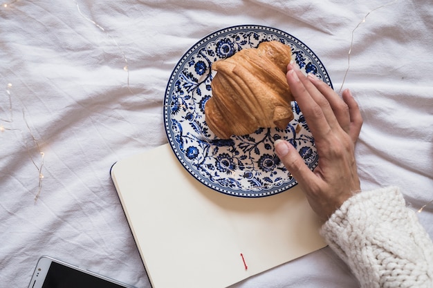 Hand touching croissant on plate