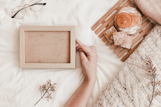 Hand touching photo frame near pastry on bed