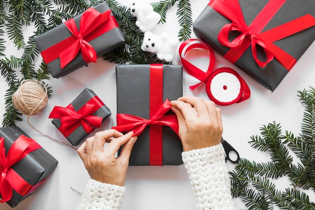 Hand tying ribbon on present box near fir twigs 