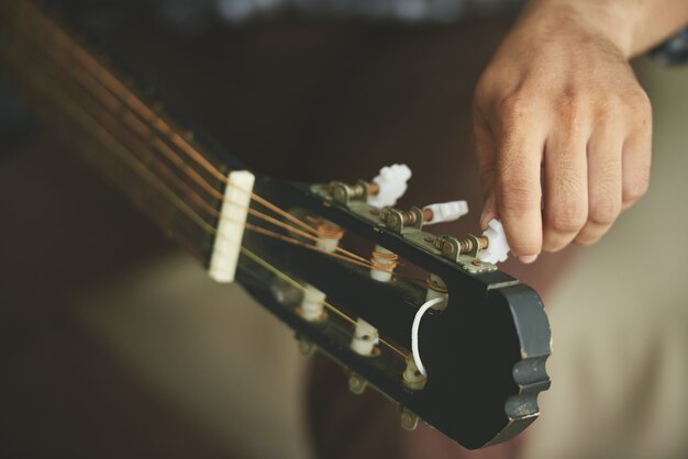 Hand of unrecognizable man turning tuning pegs of acoustic guitar
