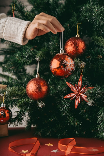 Free photo hand of unrecognizable woman holding bauble in front of christmas tree