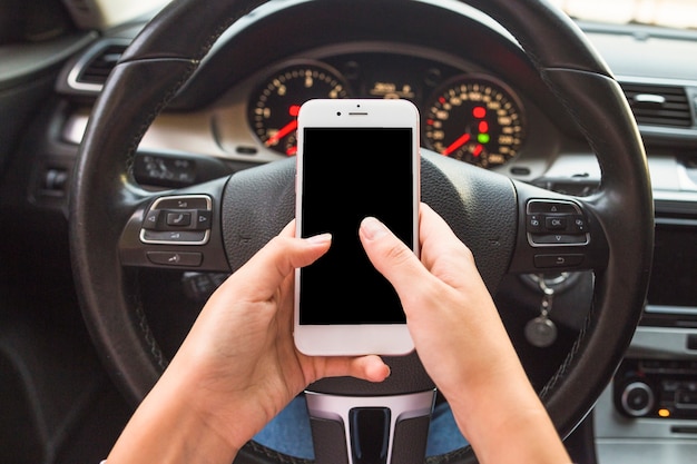 Hand using cellphone in front of steering wheel in the car