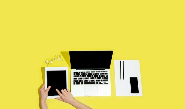 Hand using gadgets, devices on yellow background top view, blank screen with copyspace, minimalistic style. 