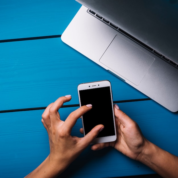 Free photo hand using smartphone above blue desk