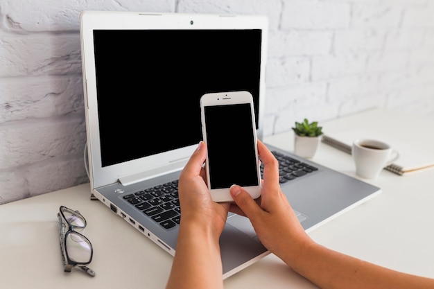 Hand using smartphone in front of open laptop over the desk