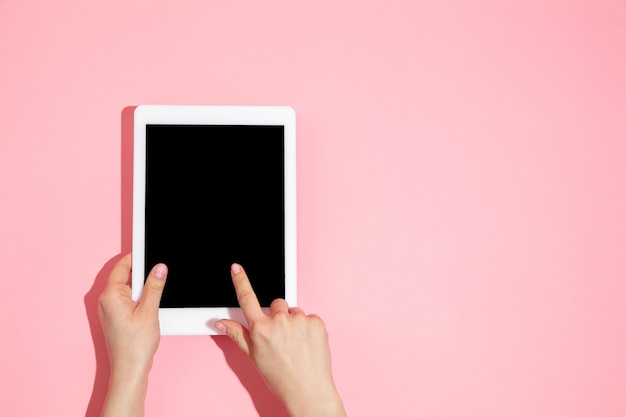 Hand using tablet, device on pink background top view, blank screen with copyspace, minimalistic style. Technologies, modern, marketing. Negative space . Coral color on wall. Stylish, trendy.