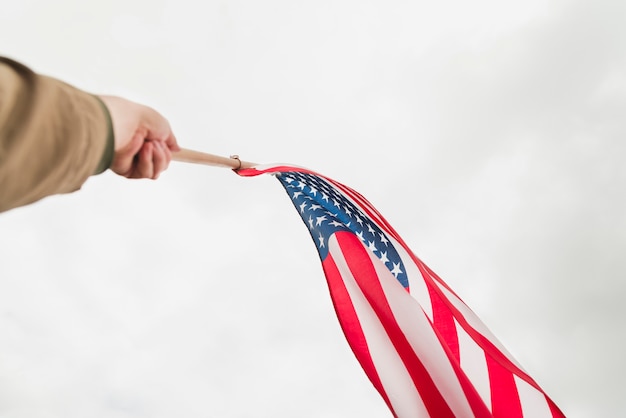 Foto gratuita mano che sventola la bandiera americana nel cielo