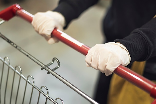 Hand wearing a latex glove while pushing a shopping cart to prevent coronavirus contamination