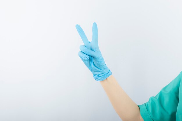 Hand wearing surgical glove and showing victory gesture. 