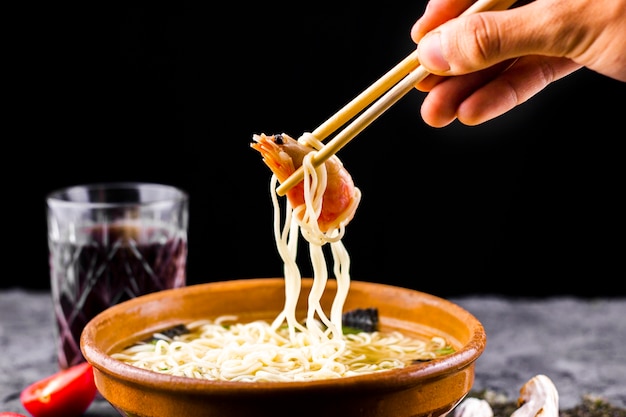 Hand with chopsticks holding shrimp noodles