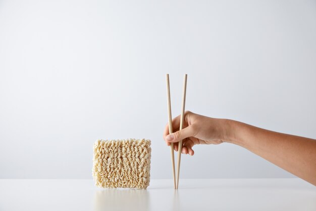 Hand with chopsticks near pack of pressed dry egg noodles isolated on white