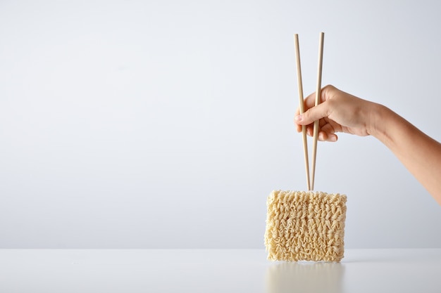 白で隔離されたプレス乾燥卵麺のパックの上に箸を持って手