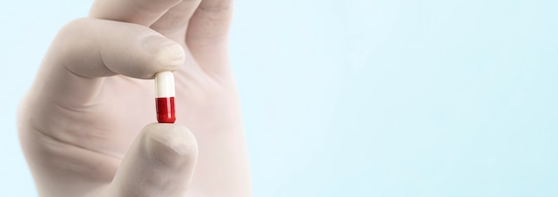 Hand with latex glove holding pill with copy space