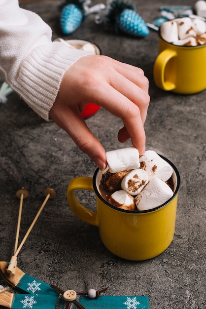 Hand with marshmallow near cup and Christmas toys 