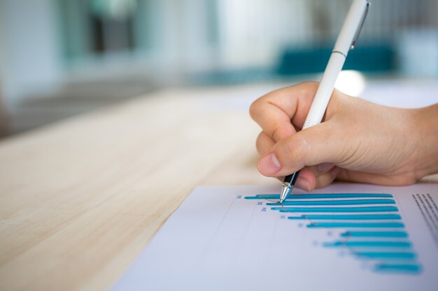 Hand with a pen writing on a paper with a bar chart