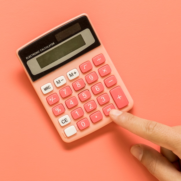 Hand with pink calculator on colored surface