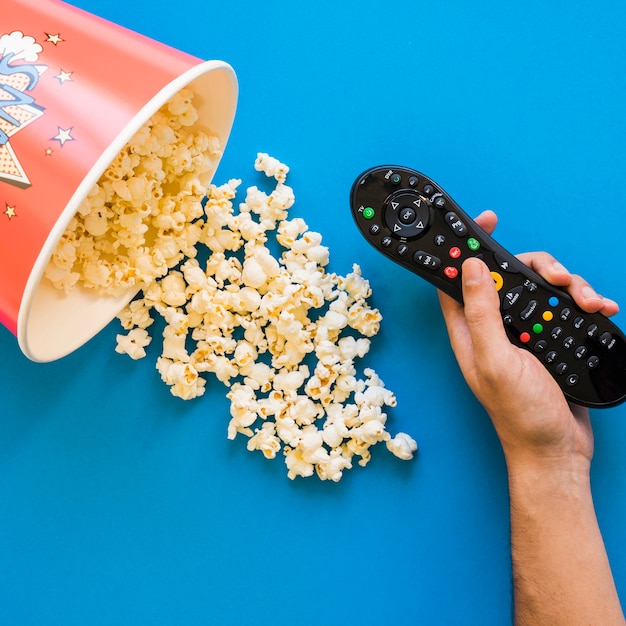 Hand with remote control and bucket of popcorn