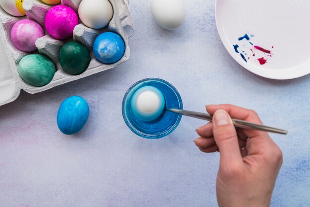 Hand with spoon near glass of water and Easter eggs in container