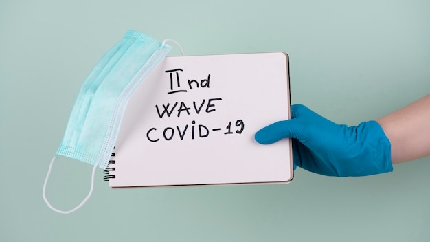 Free photo hand with surgical glove holding notebook saying second wave of covid