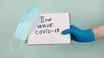 Free photo hand with surgical glove holding notebook saying second wave of covid