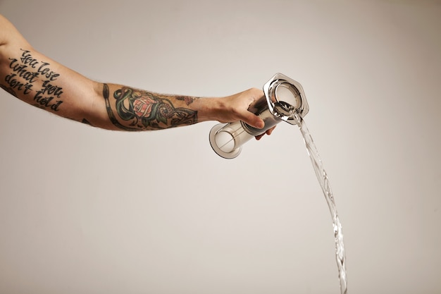 Free photo hand with tattoos holding aeropress, water pouring out of aeropress on white alternative coffee brewing commercial