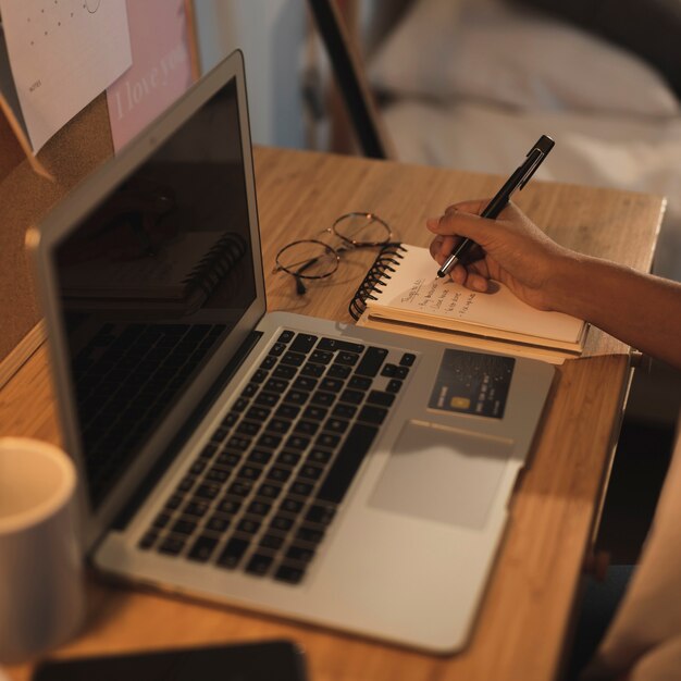 Hand writing in a notebook next to a laptop