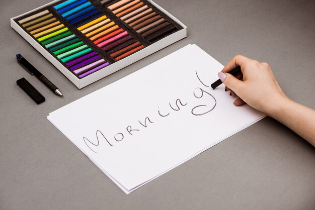 Рука, пишущая слово утро на бумаге с пастельными мелками