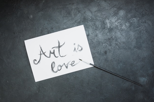 Hand written 'art is love' text on white paper with paint brush over slate surface