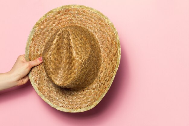 Hand of young woman holding summer straw hat on pink background. Fashion Background. Summer Concept.