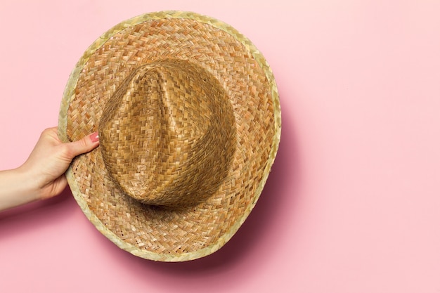 분홍색 배경에 여름 밀 짚 모자를 들고 젊은 여자의 손. 패션 배경. 여름 개념.
