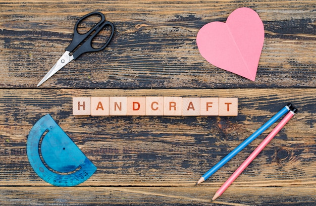 Free photo handcraft and hobby concept with wooden cubes, tools, cut heart paper on wooden background flat lay.