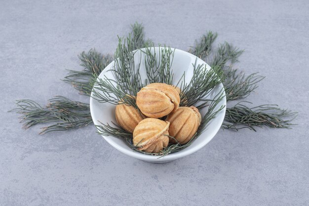 Handful of caramel filled cookies adorned with pine leaves on marble table.