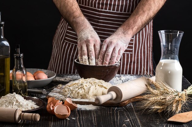 A handful of flour with egg on a rustic kitchen. Against the background of men's hands knead the dough. Ingredients for cooking flour products or dough bread, muffins, pie, pizza dough . Copy space