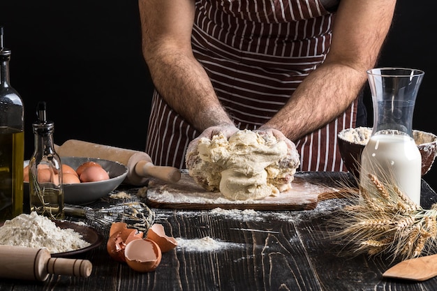 A handful of flour with egg on a rustic kitchen. Against the background of men's hands knead the dough. Ingredients for cooking flour products or dough bread, muffins, pie, pizza dough . Copy space