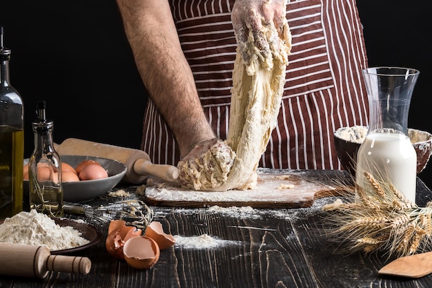 Горсть муки с яйцом на деревенской кухне. На фоне мужские руки месят тесто. Ингредиенты для приготовления мучных изделий или теста для хлеба, кексов, пирогов, теста для пиццы. Копировать пространство