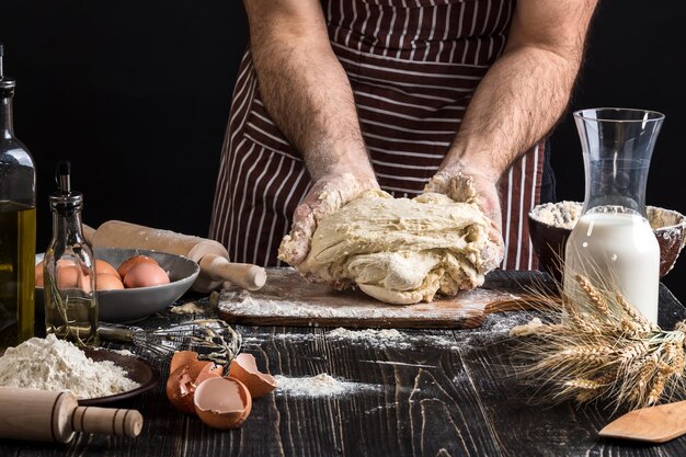 A handful of flour with egg on a rustic kitchen. Against the background of men's hands knead the dough. Ingredients for cooking flour products or dough bread, muffins, pie, pizza dough . Copy space