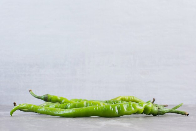 A handful of green peppers on marble.