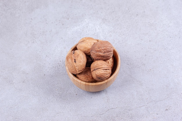 A handful of walnuts piled in a wooden bowl on marble surface