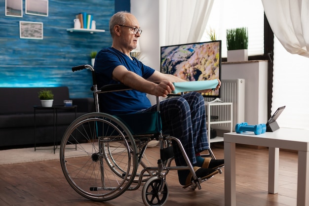 Старик-инвалид в инвалидной коляске тренирует сопротивление рук, тренируя мышцы тела
