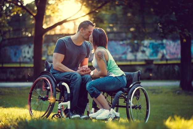 Handicapped young couple on two wheelchairs kissing in autumn park.