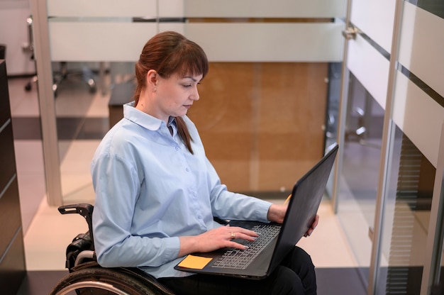 С ограниченными возможностями молодая женщина в офисе работает на ноутбуке